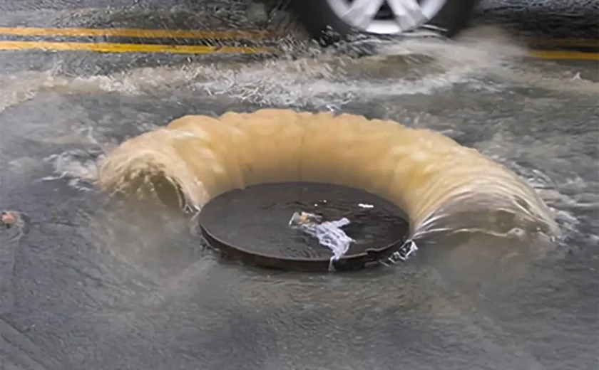 depicting a drainage system struggling to cope with heavy rain, showing water pooling on the surface due to overwhelmed drains. The scene highlights the challenges of managing excessive rainfall, with visible water accumulation and potential flooding in the area