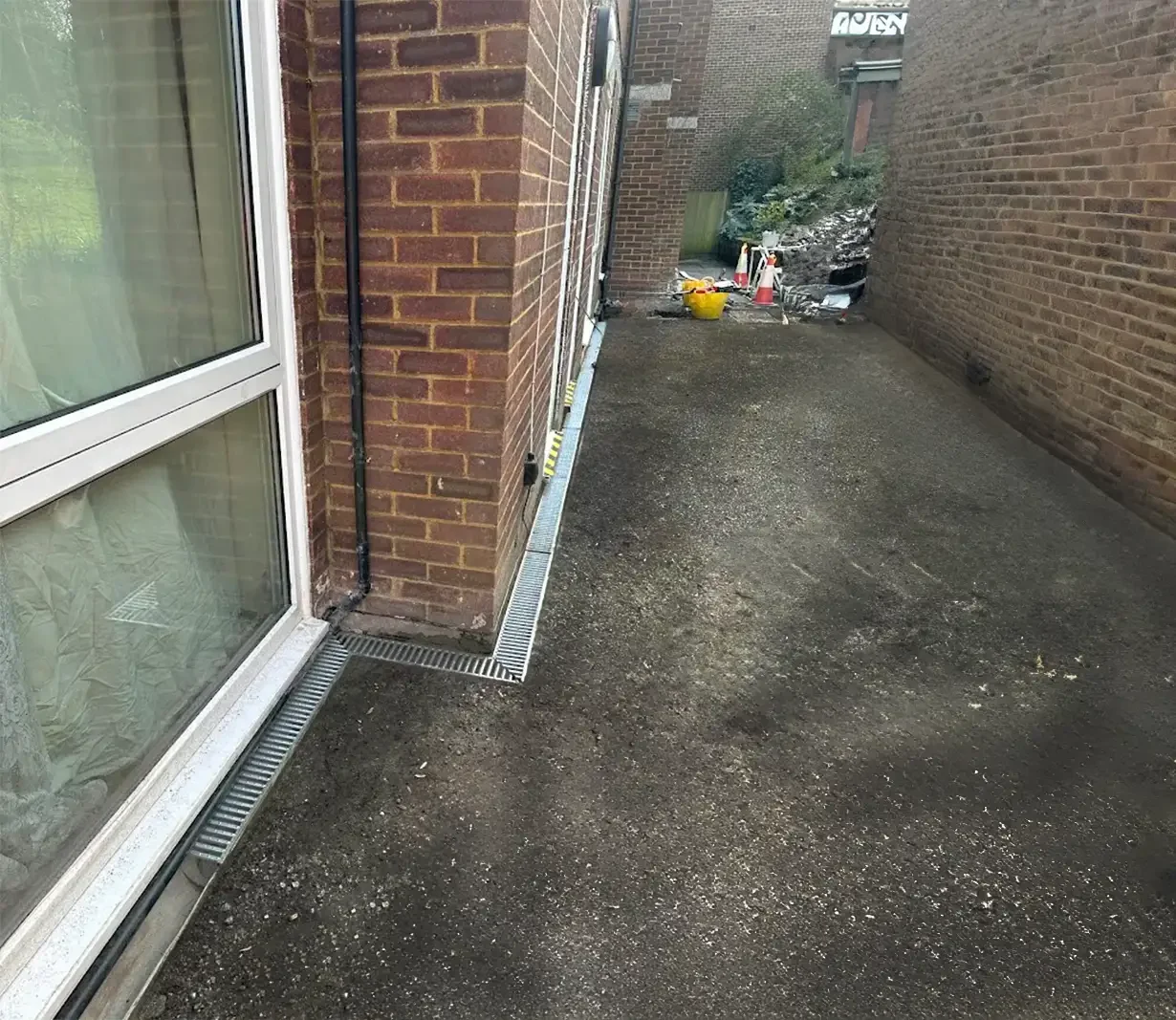 recently installed EcoDrain system running along the edge of a building, extending from one end to the other. The drainage system is aligned with the tarmac level, optimized to efficiently manage and direct the flow of heavy rainfall.